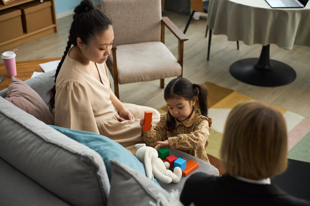 two woman watching a girl play with blocks on the sofa