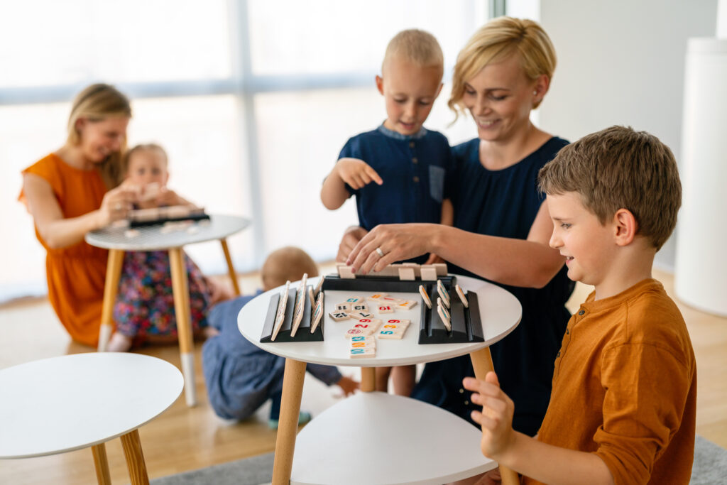 Women at the table playing board game with children. Family, nursery, childhood concept.