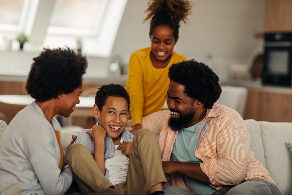 Afro parents and their children are socializing while sitting on the sofa in the living room