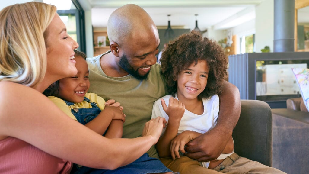 Portrait Of Smiling Family Hugging And Sitting On Sofa At Home Together